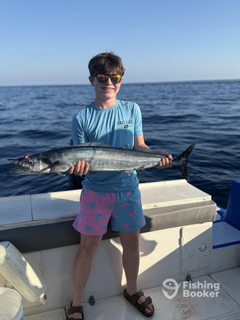 Young angler proudly holding a large fish while fishing offshore, showcasing a beautiful day on the water.