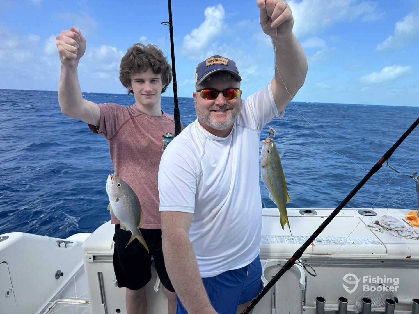 A father and son duo proudly displaying their catches of Yellowtail Snapper while fishing in open waters.