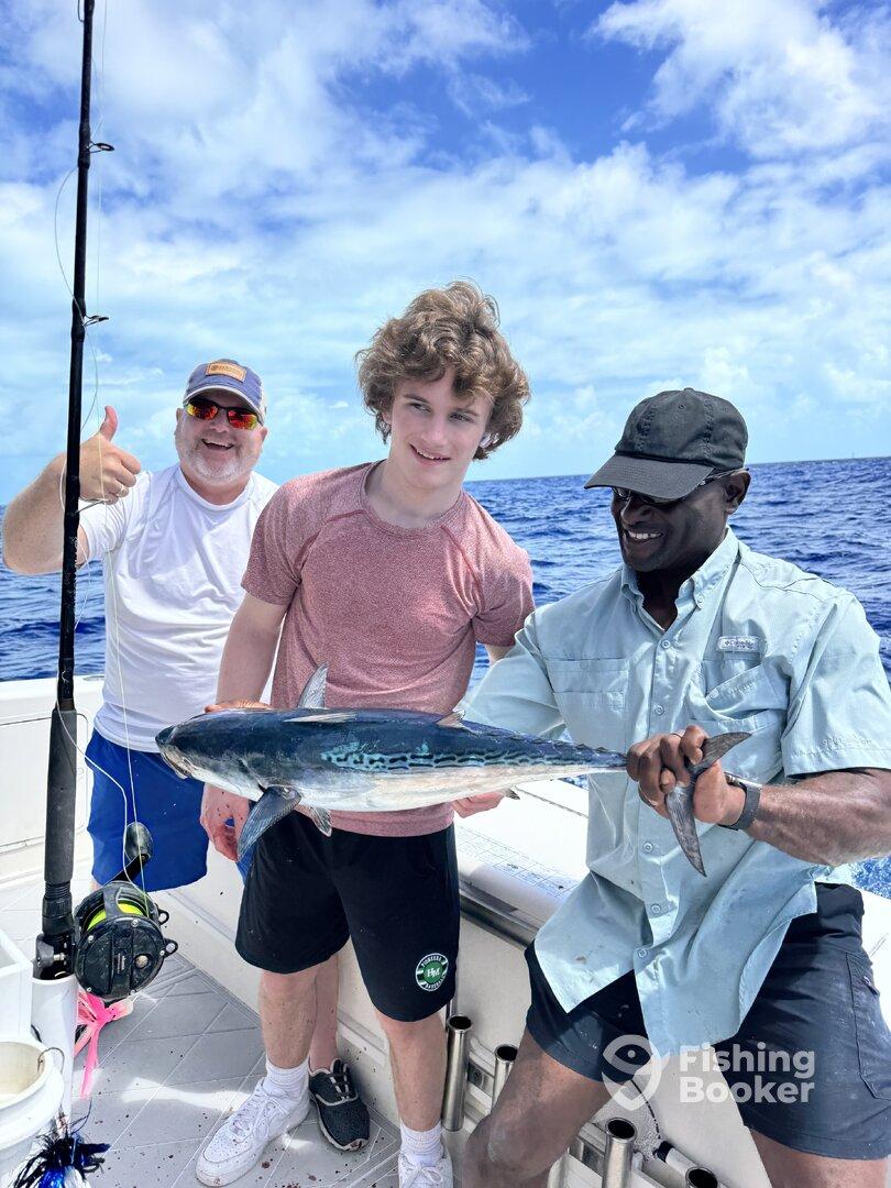 A young angler proudly displays a caught fish alongside two adults on a fishing charter, enjoying a day out on the open water.