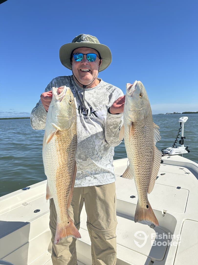Angler proudly displaying two large Redfish while enjoying a sunny day on the water.