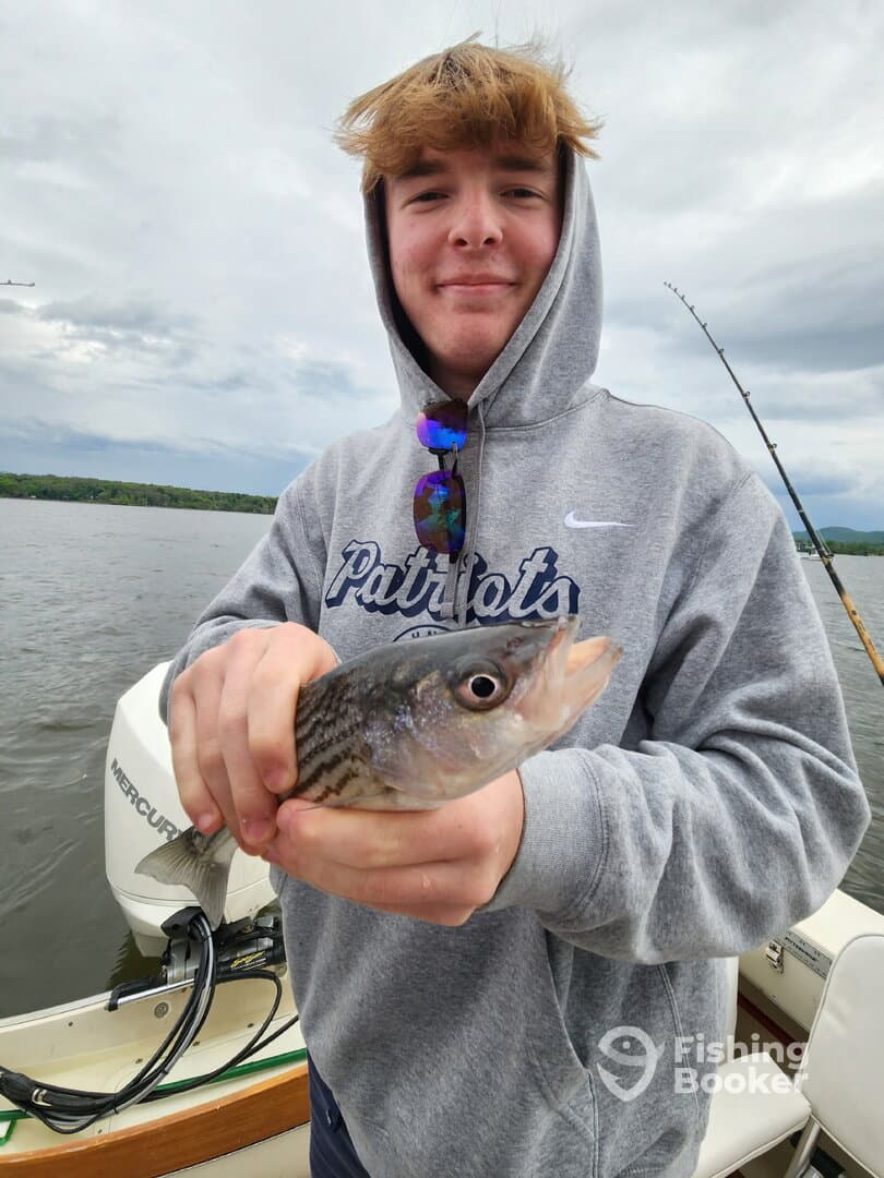 A young angler proudly displaying a striped bass while fishing on a calm lake, showcasing a relaxed day on the water.