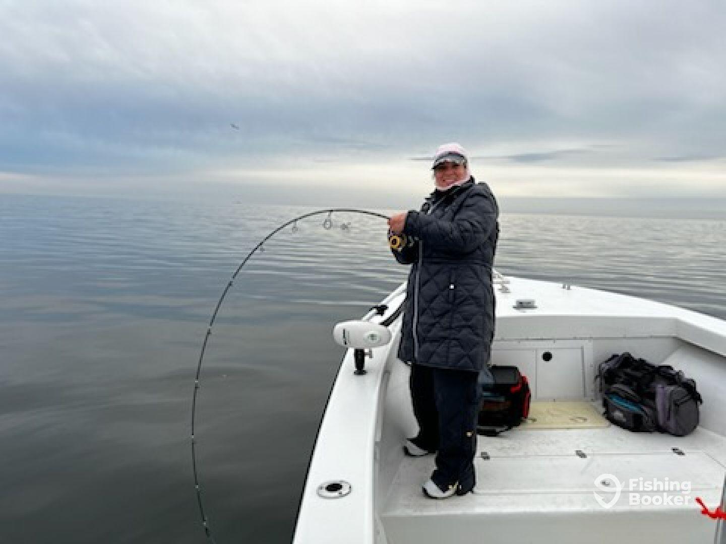 An angler reeling in a catch while fishing on a calm day in open waters, showcasing the excitement of the sport.