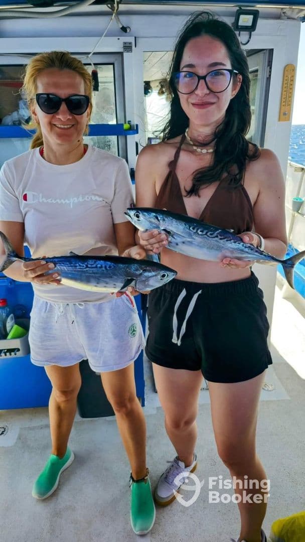 Two anglers proudly displaying their catch of Mackerel aboard a fishing boat, enjoying a sunny day on the water.