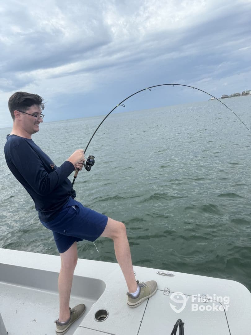A young angler actively reeling in a fish while fishing from a boat in a coastal environment, showcasing the excitement of the catch.
