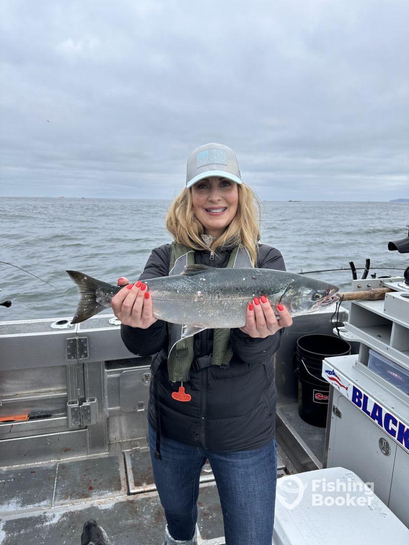 An angler proudly displaying a freshly caught Salmon aboard a fishing boat in a coastal setting.