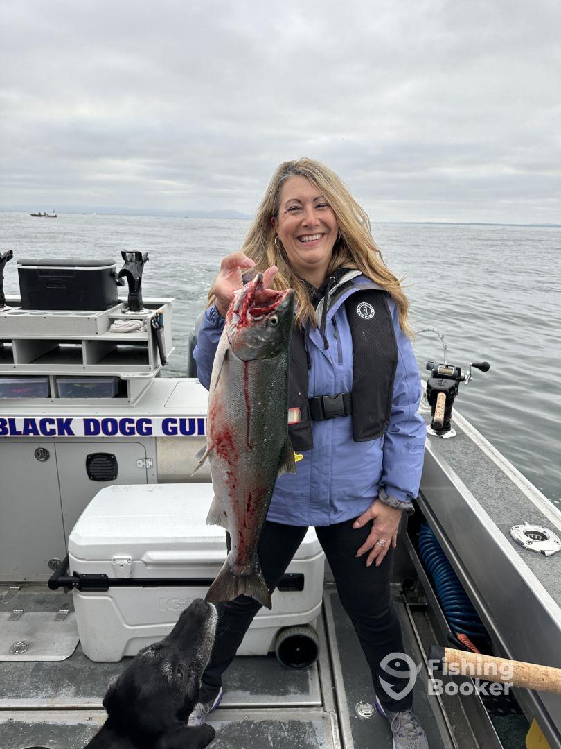 A smiling angler proudly displays a freshly caught Salmon while fishing on a boat, showcasing the excitement of a successful fishing trip.