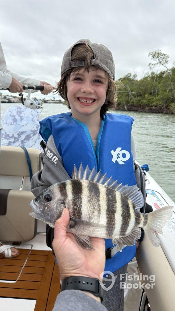 A young angler proudly displaying a Sheepshead fish while enjoying a fishing trip on a boat.