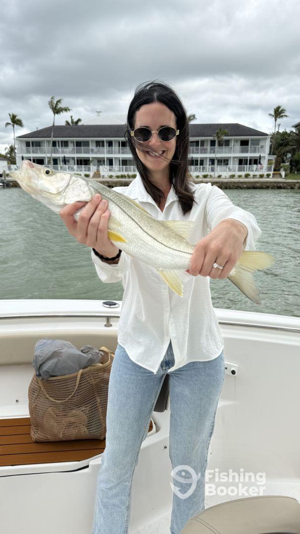 Angler proudly displaying a Snook caught while fishing from a boat in a coastal waterway.