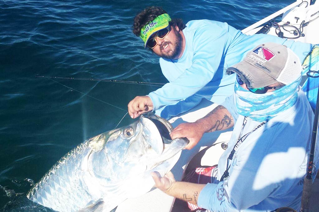 Two anglers on the edge of a boat holding a Tarpon by the mouth