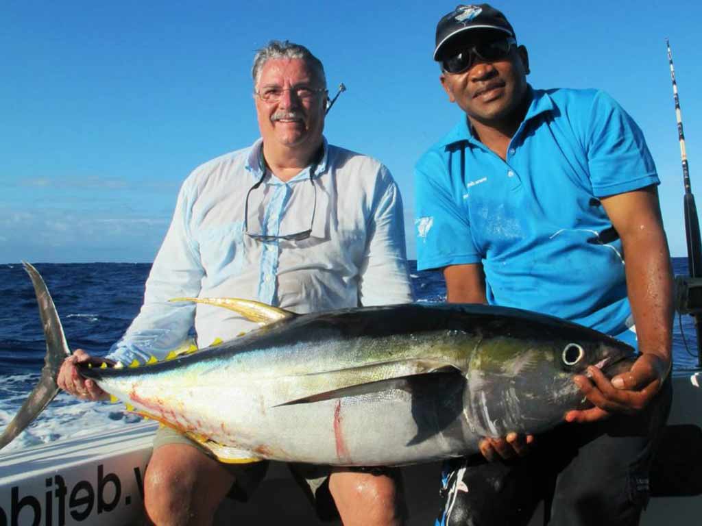 Two anglers displaying a Yellowfin Tuna caught on a charter boat in the Maldives while sitting on the side of the boat on a sunny day