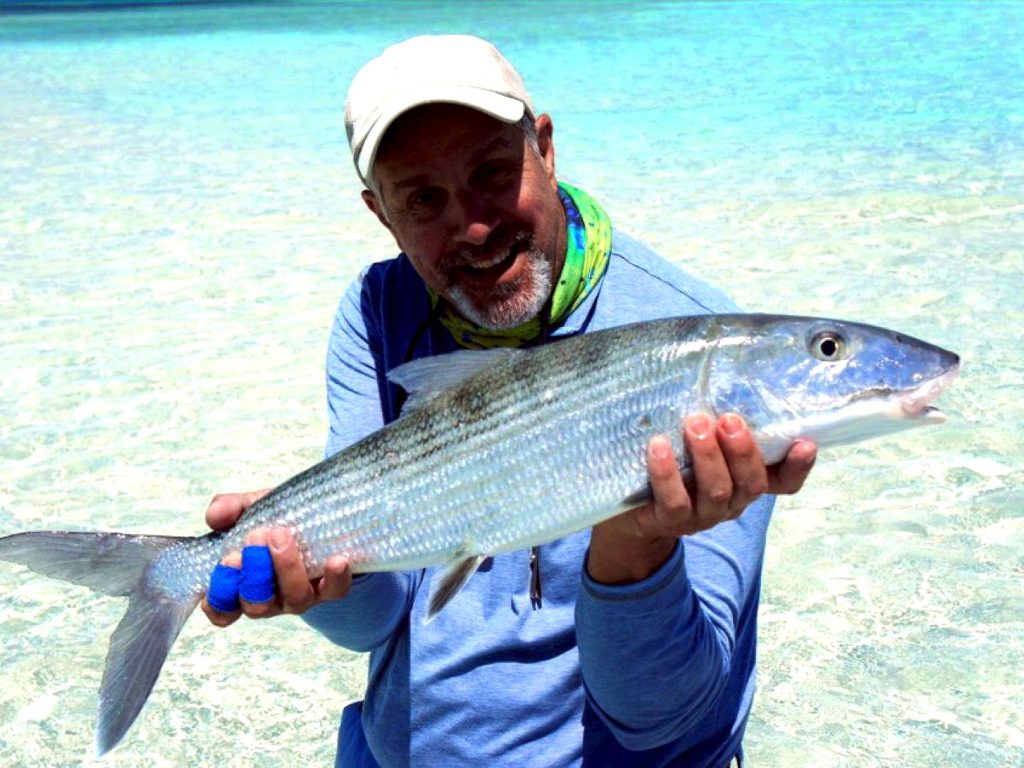 Мужчина держит Bonefish в мелководье на берегу