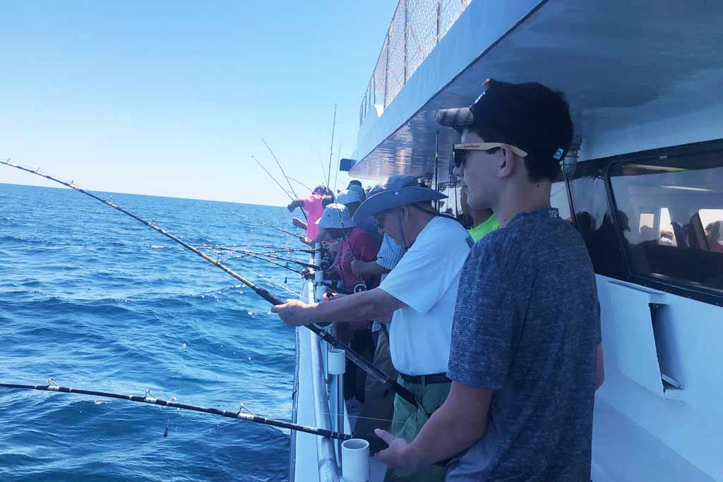 Anglers lined up against the side of a party boat, all holding their fishing rods