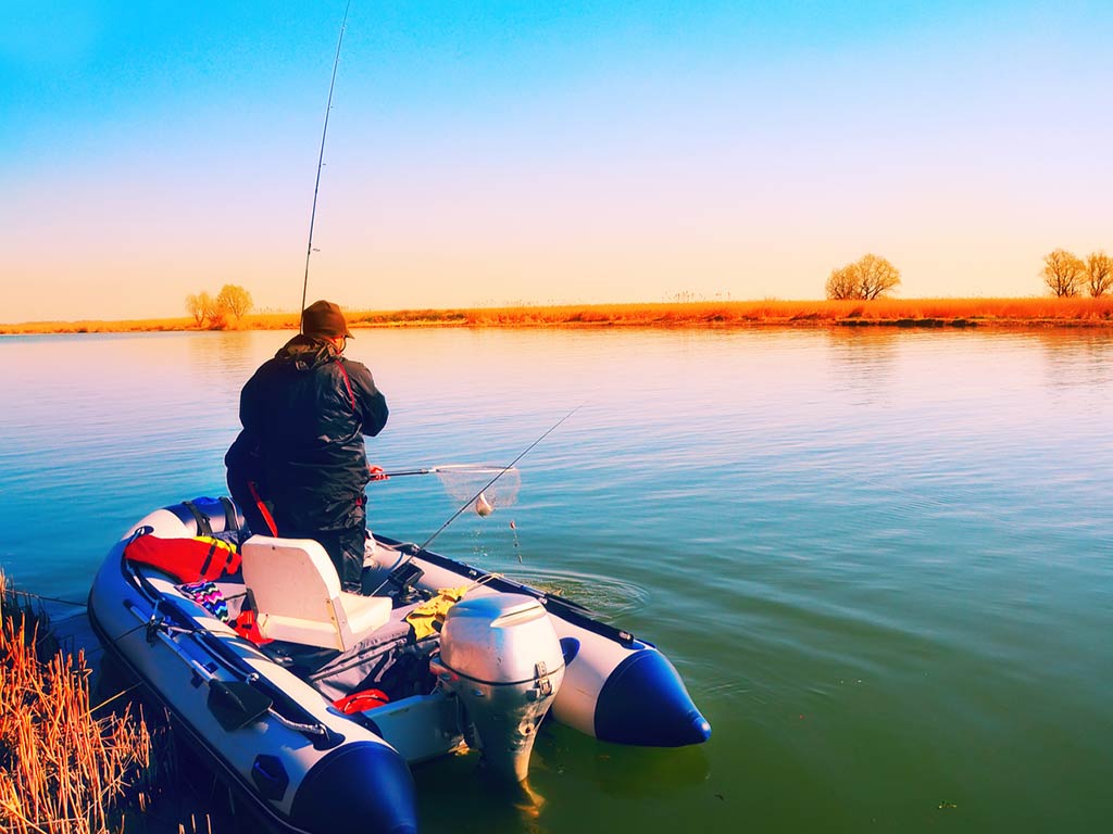 A photo of an angler fishing from a inflatable boat during a sunset