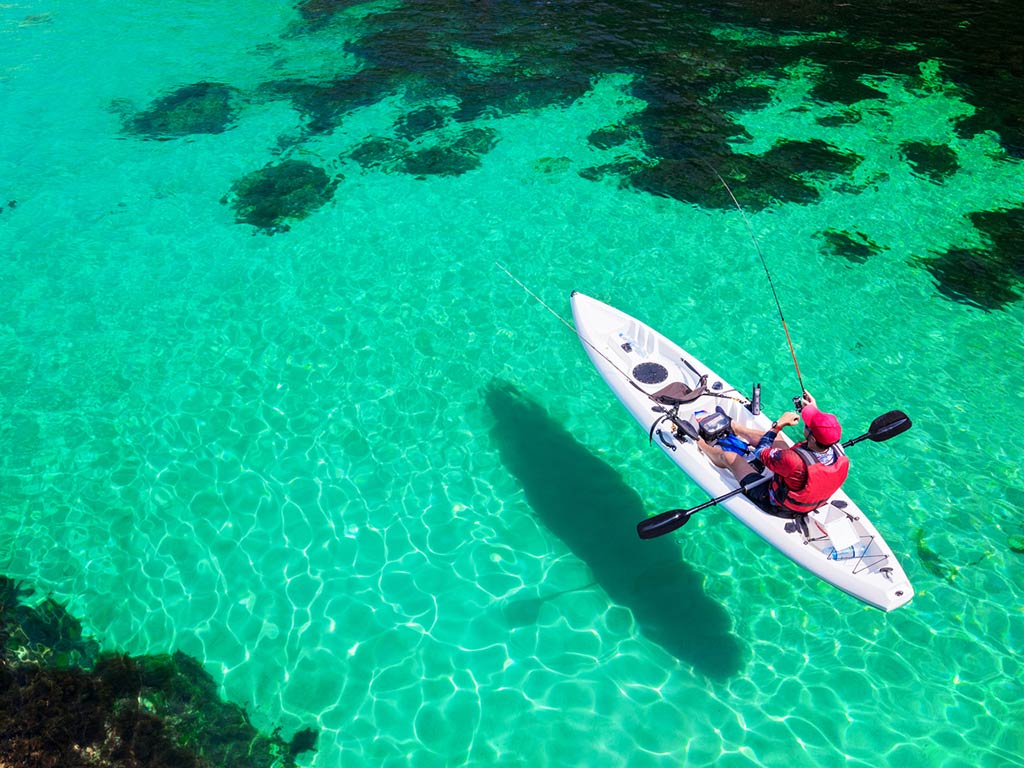 An aerial view of an angler in a kayak while fishing in the crystal clear turquoise water