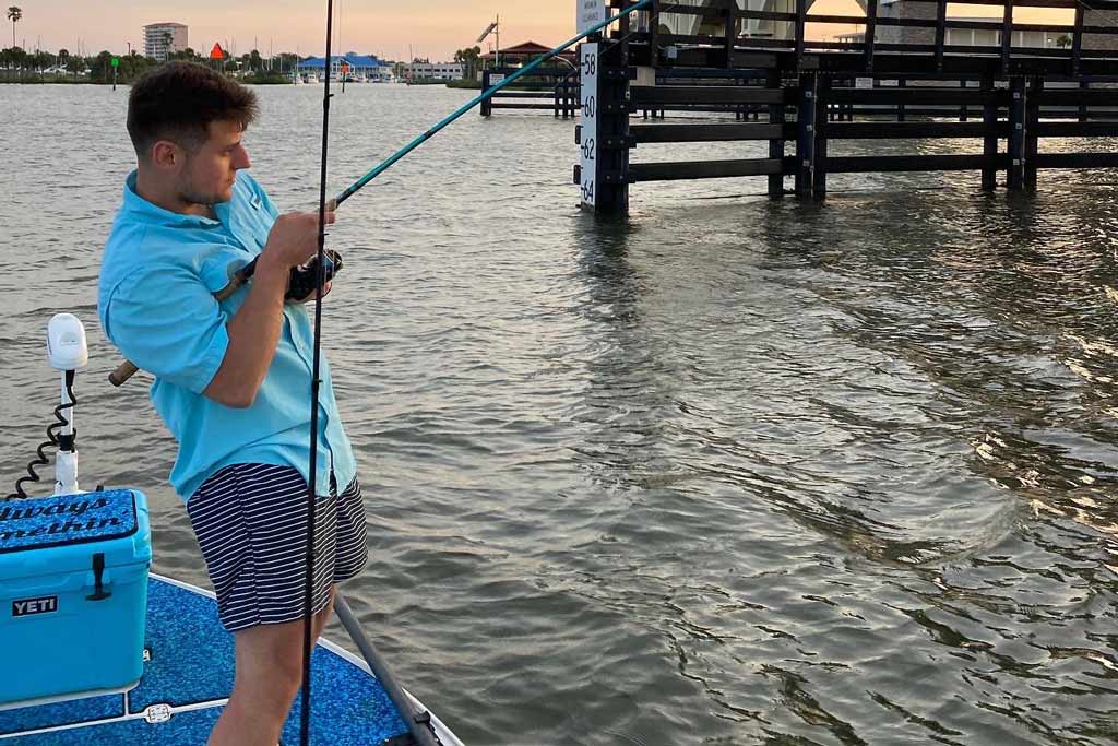 A young man in a blue shirt standing on a fishing boat, fishing near bridge pylons