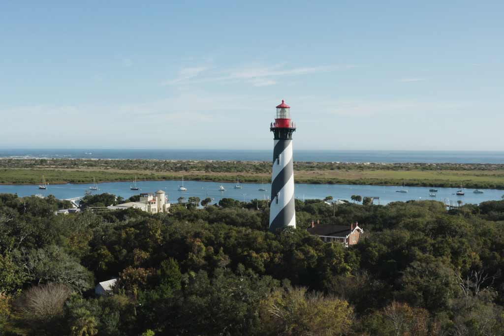 An aerial view of the St. Augustine Lighthouse surrounded by greenery, with water and open in far in the background