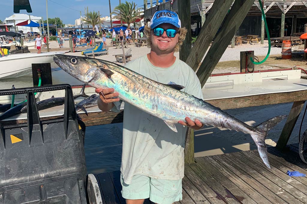 A smiling angler standing on a dock, holding a big King Mackerel