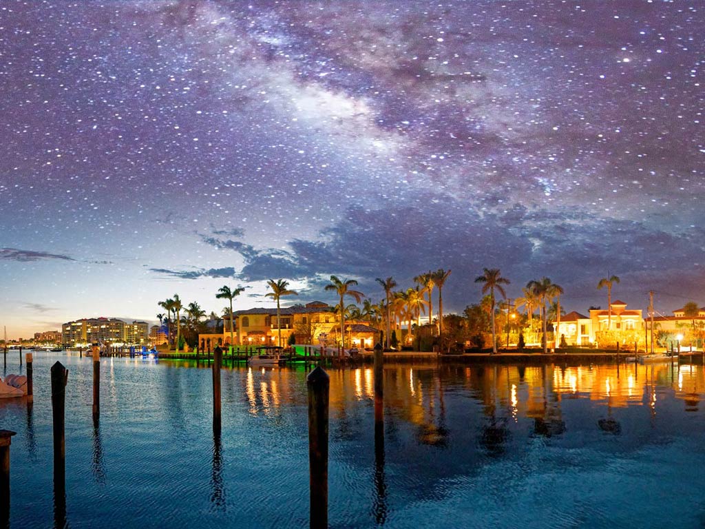 A view of Boca Raton from the water at night, with houses lit up on the waterfront and a starry sky above
