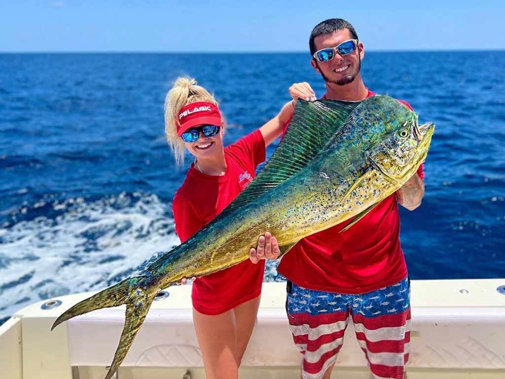 A photo of two anglers in matching clothes inspired with the US flag patterns standing on a charter boat and posing with big Mahi Mahi