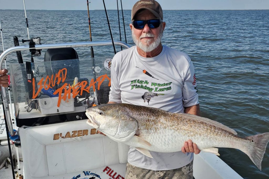 An angler on a boat, with spinning rods set up behind him, holding a Redfish.