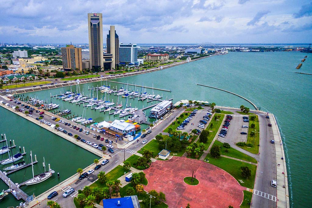 An aerial view of the City Harbor in Corpus Christi, with the marina in the foreground and some taller buildings in the background