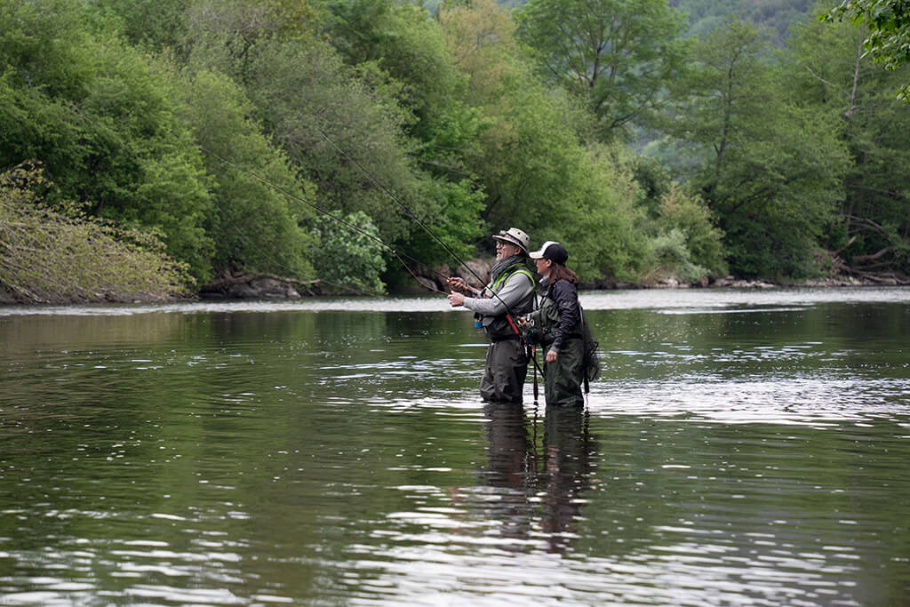 A father and daughter fly fishing together in a shallow river