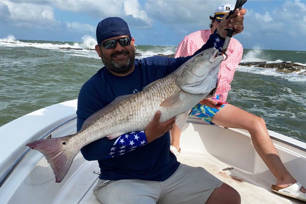 A smiling angler holding a large Redfish aboard a charter boat.