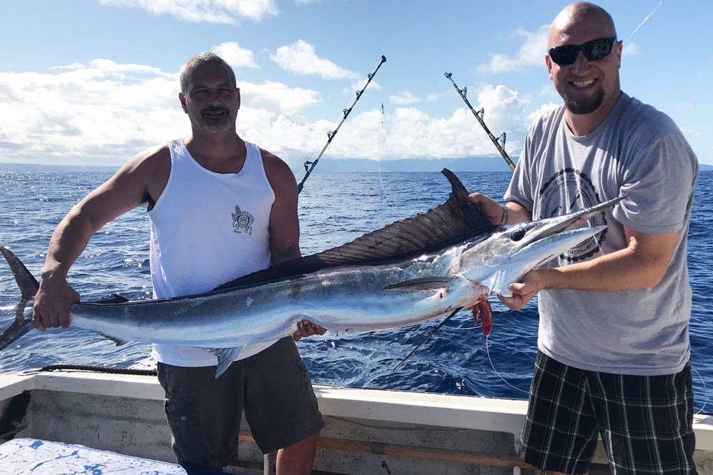 Two smiling anglers standing on a boat, holding a Striped Marlin, with water and blue skies in the background