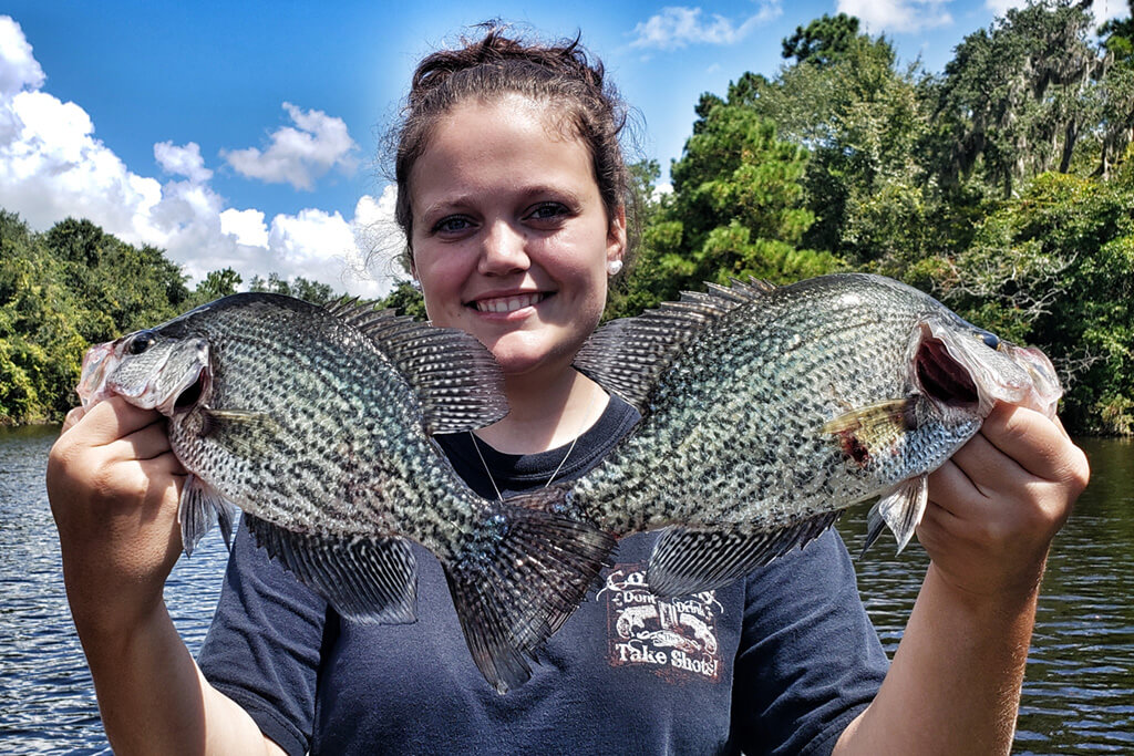 een jonge vrouw met twee grote zwarte Crappie met een meer achter haar