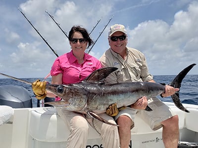 A couple sitting on a charter fishing boat with a large swordfish on their lap