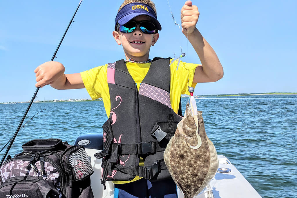 Un niño feliz sosteniendo una platija que atrapó con un señuelo de plástico blando