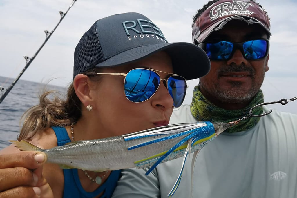 A man and a woman posing with a ballyhoo fishing bait rigged with a trolling header lure