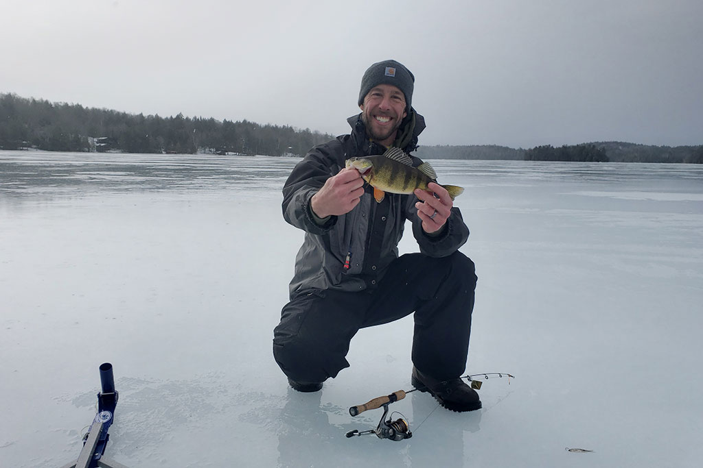 A smiling angler holds a Perch caught while ice fishing.