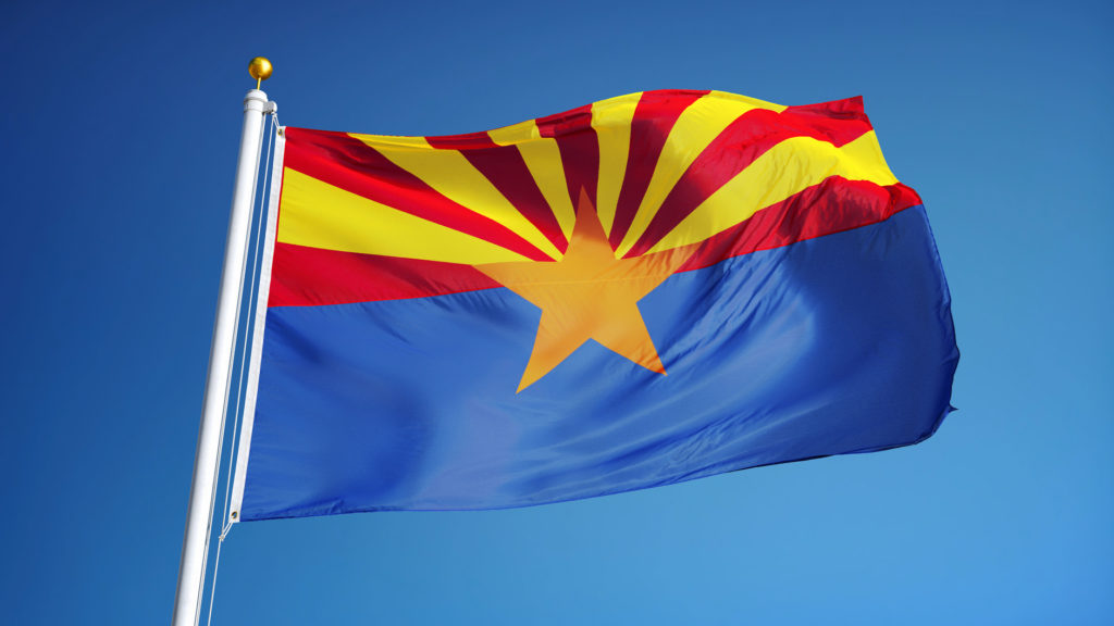 The state flag of Arizona blowing in the wind on a flagpole against clear blue sky
