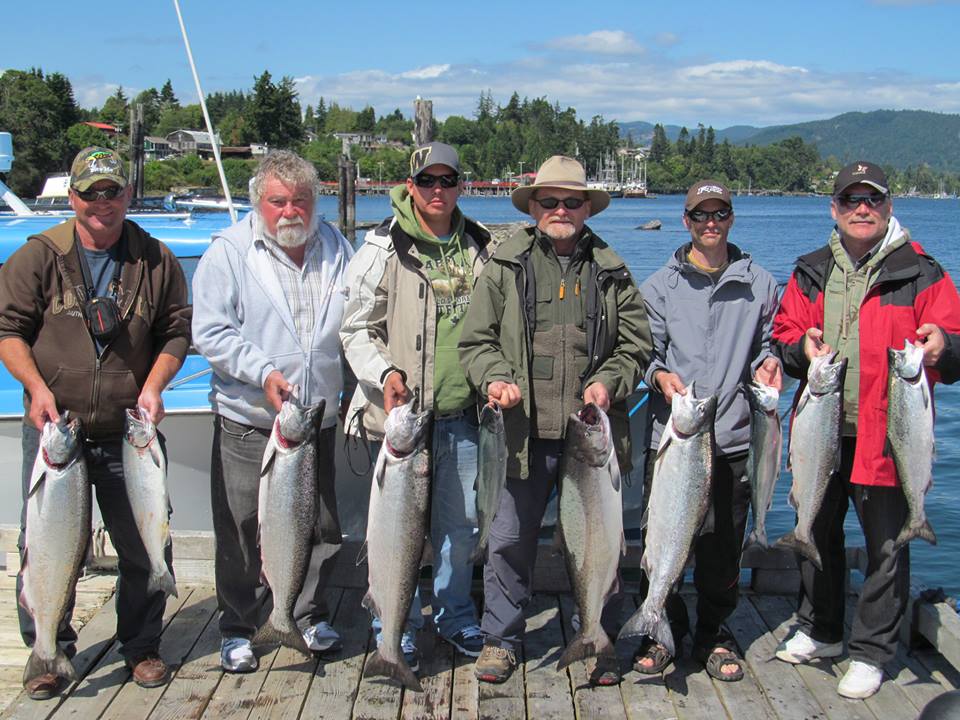 Six anglers standing on a dock behind a boat holding Salmon caught while fishing in Vancouver Island with Top Rods Guide Service