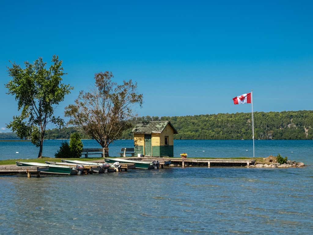 A photo of Manitoulin Island on Lake Huron, featuring a pier with a small house and the Canadian flag flying.