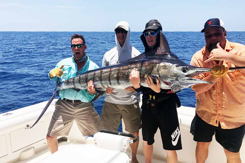 Four anglers standing on a boat, holding a big Marlin they just caught