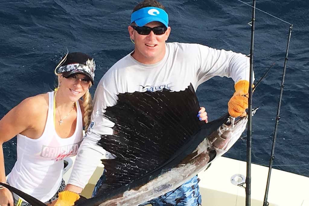 A man and a woman standing on a boat, holding a Sailfish