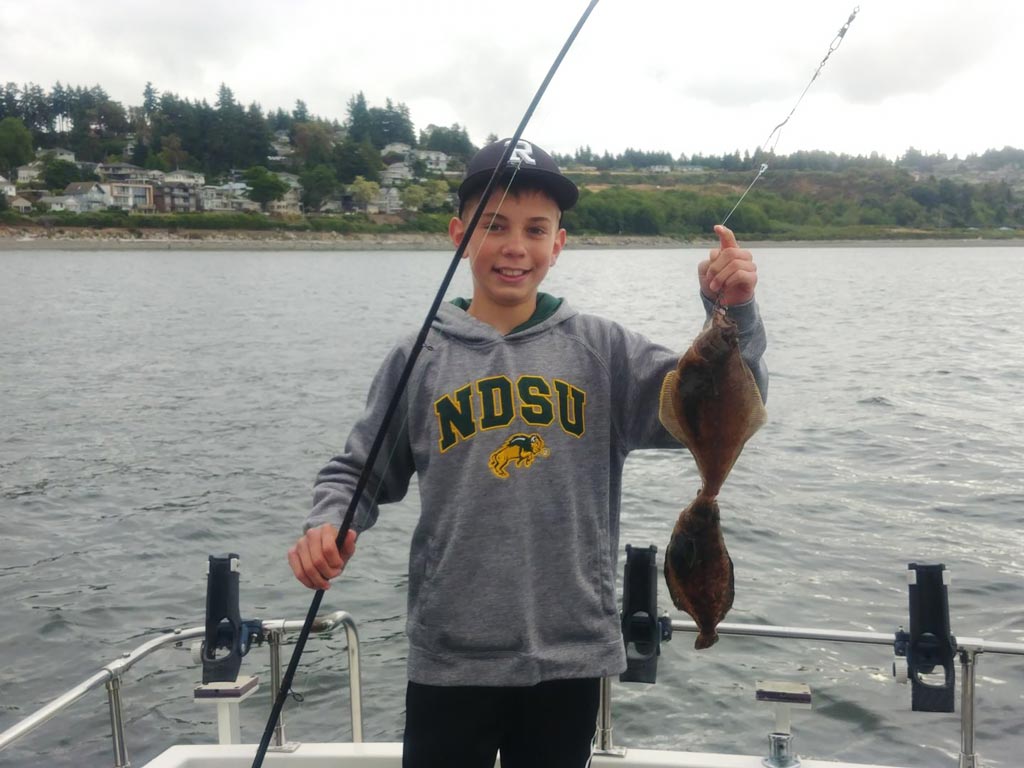 A boy holding a fishing rod and two Flounder he caught.