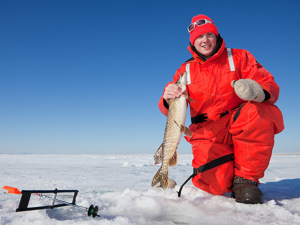 An ice fisherman smiles while raising up a fish he just reeled in.