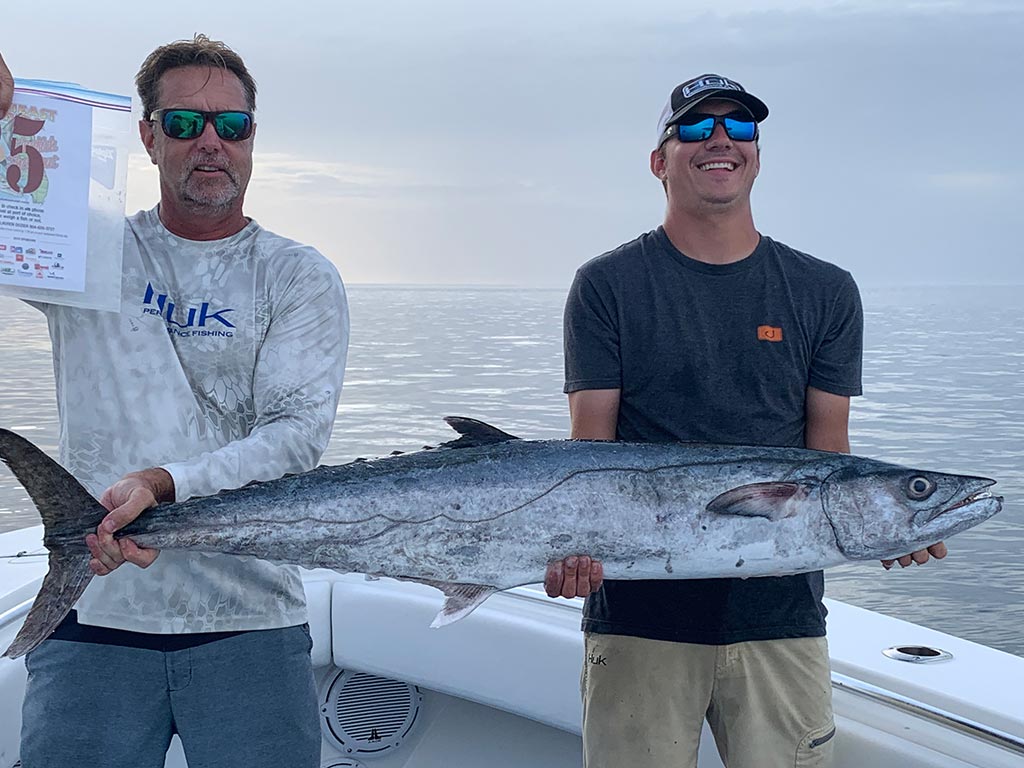 Two anglers on a boat hold a Kingfish they recently reeled in.