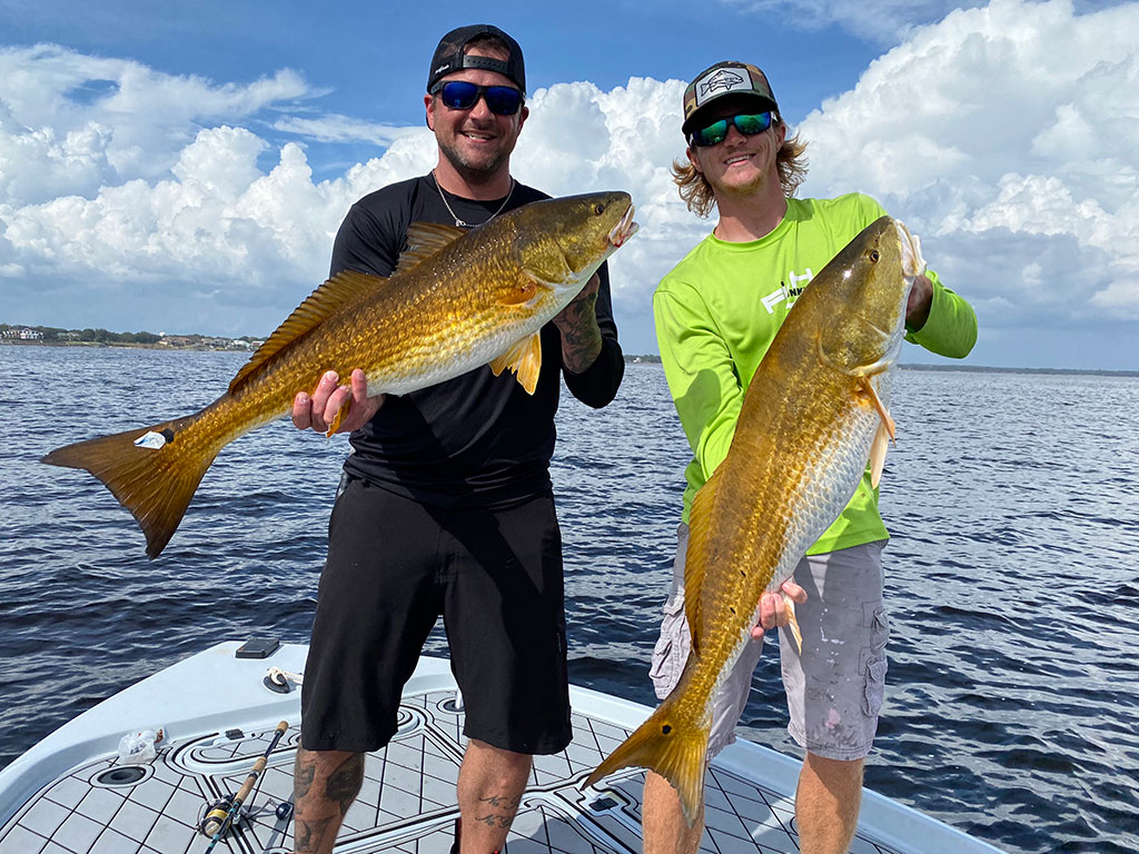 Two anglers hold a large Redfish each following a successful inshore fishing trip