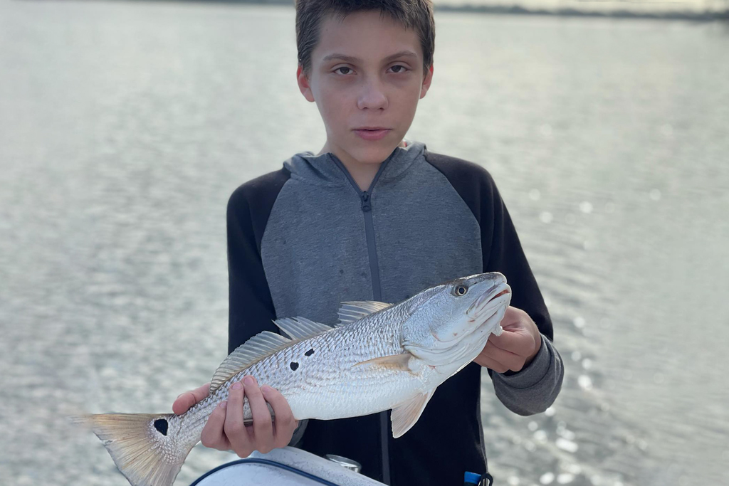 A child aboard Captain Cole's charter holds a Redfish with the water behind him