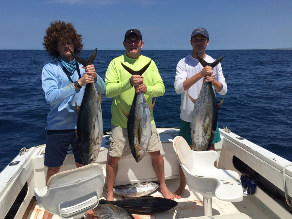 Three anglers standing on a boat with freshly caught Tuna and the sea on the background. Captain Jerry's Watersports, the Cayman Islands,