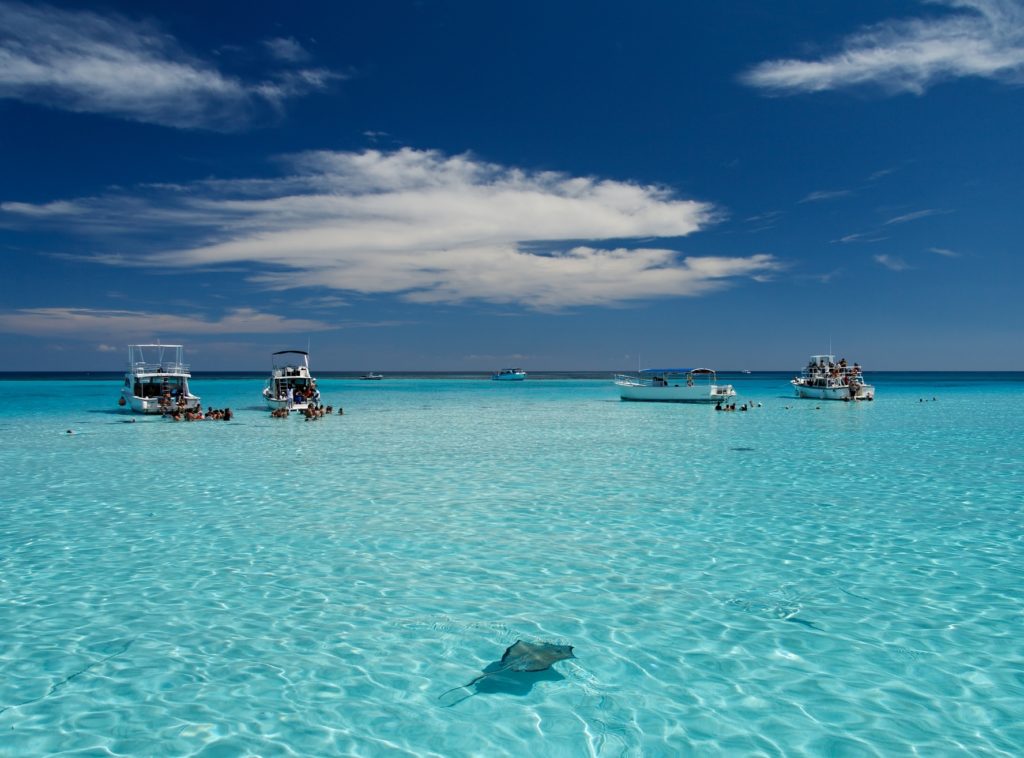 Blue Caribbean waters with stingrays and boats.
