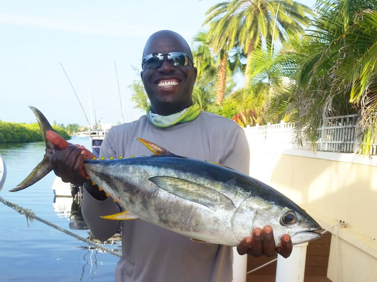 A smiling angler holding a freshly caught Tuna with Happy Day Charters, the Cayman Islands.