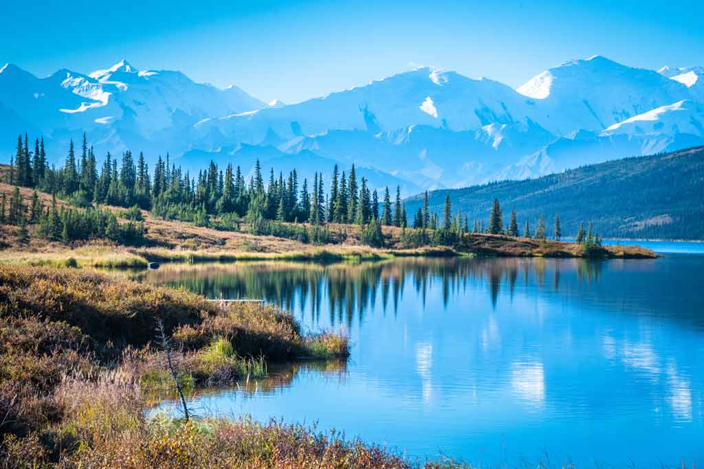 An Alaskan landscape with water, woods, and mountains in the background