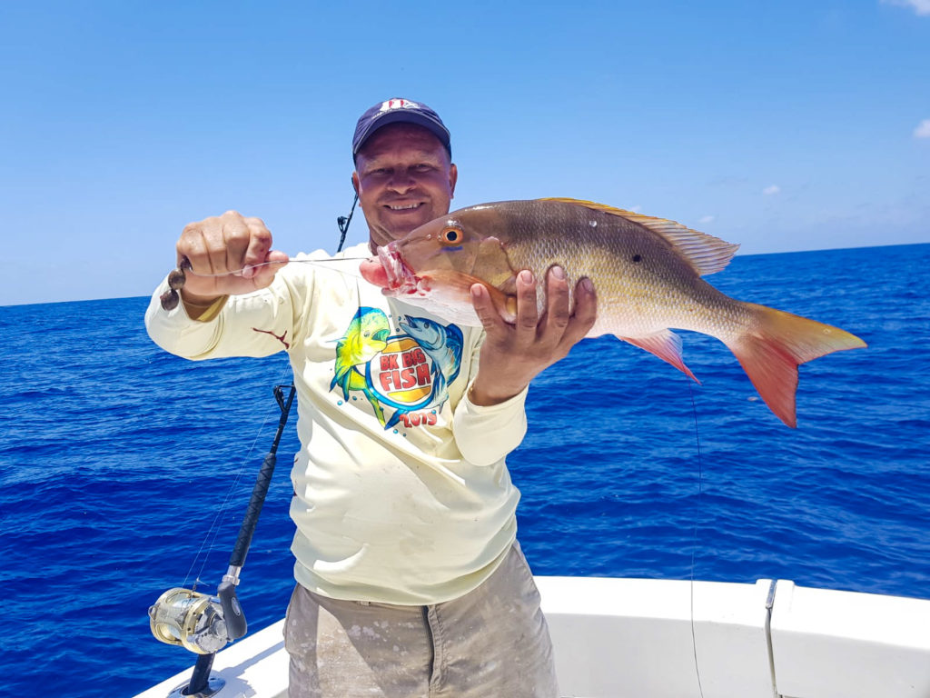 A smiling angler holding a Snapper on a boat with Infinity Private Charters in the Cayman Islands.