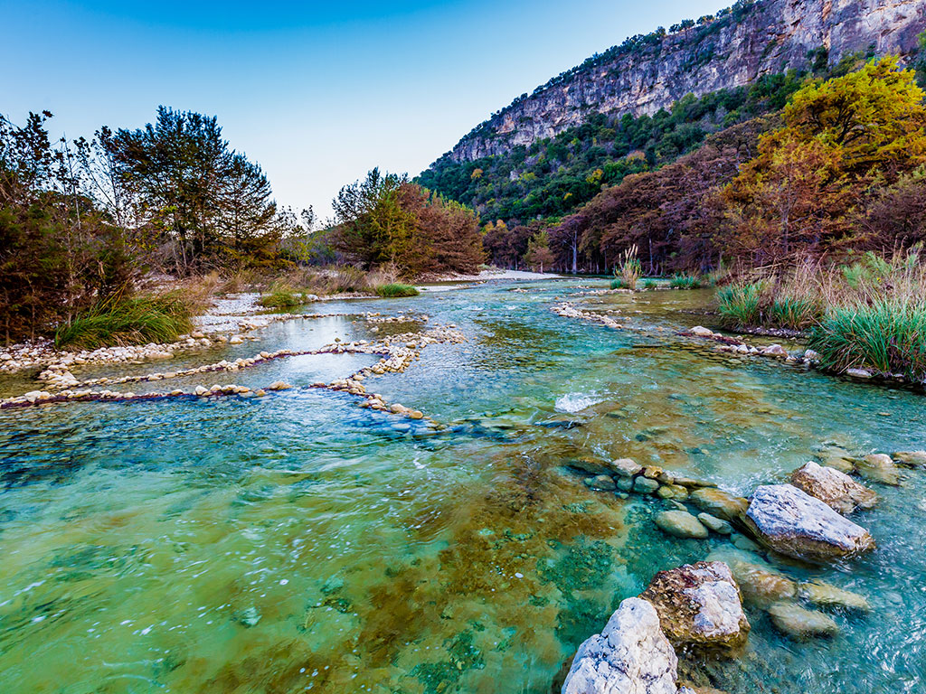 Crystal clear waters flow between rolling hills in the Texas Hill Country in spring