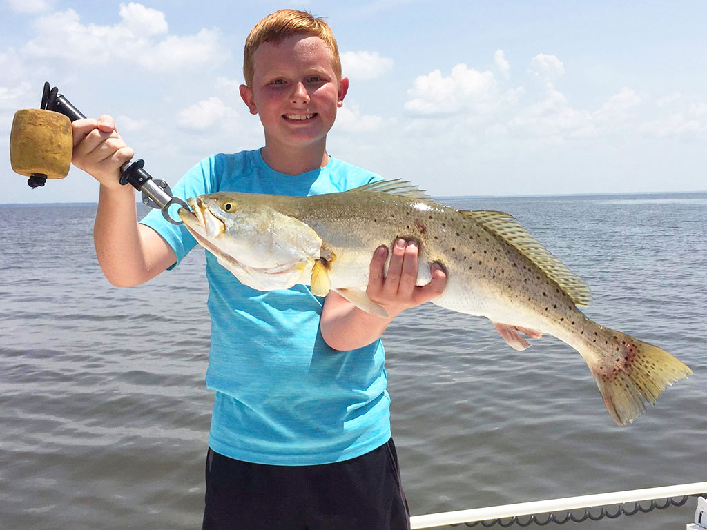 Un joven pescador sostiene una trucha manchada capturada pescando en la costa en Destin, FL.